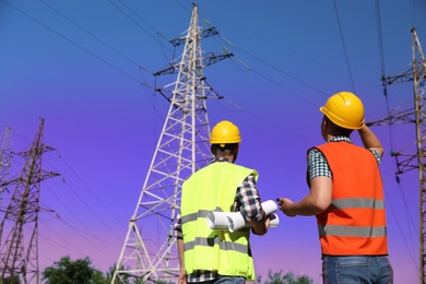 Professional electricians in uniforms near high voltage towers