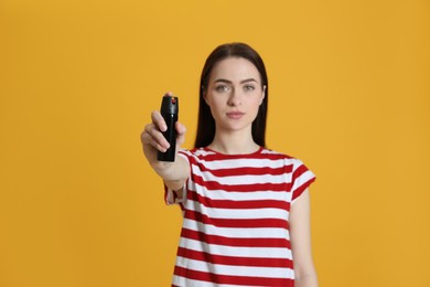 Young woman using pepper spray on yellow background