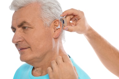 Young man putting hearing aid in father's ear on white background