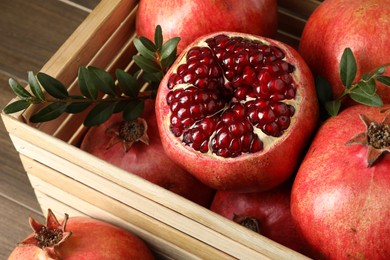 Ripe pomegranates in wooden crate on table, closeup
