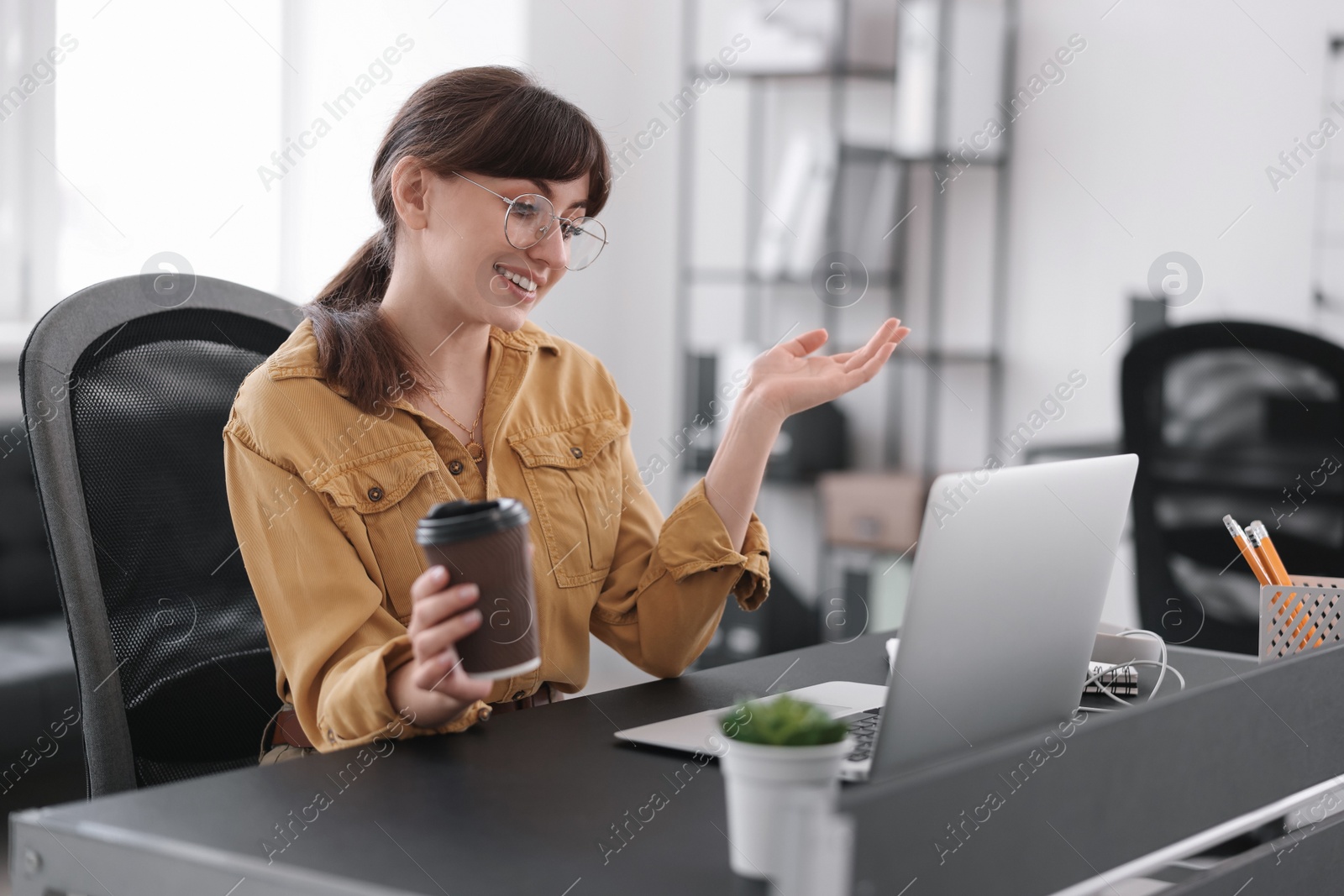 Photo of Woman with cup of coffee watching webinar at table in office