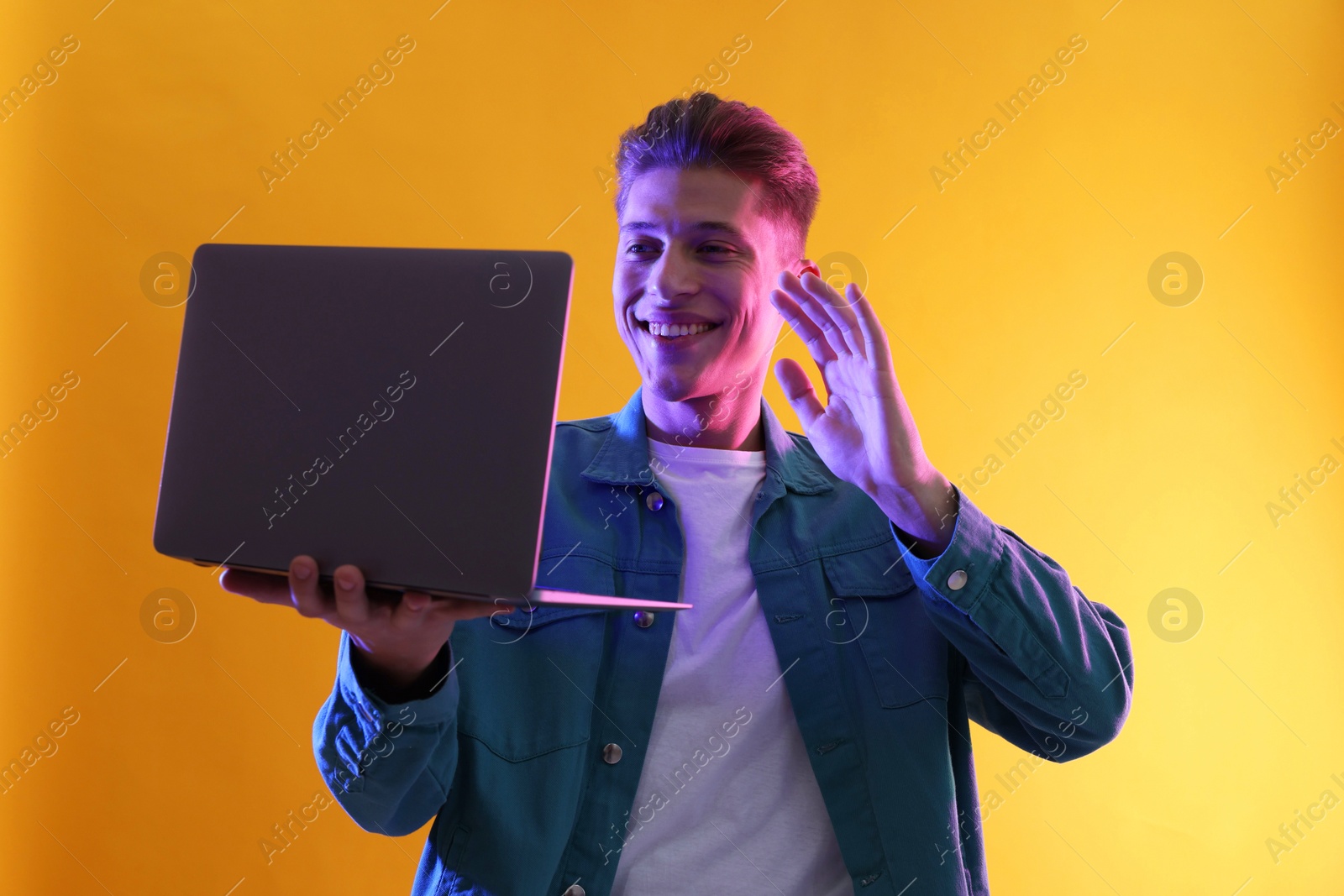 Photo of Young man with laptop talking via video chat on yellow background