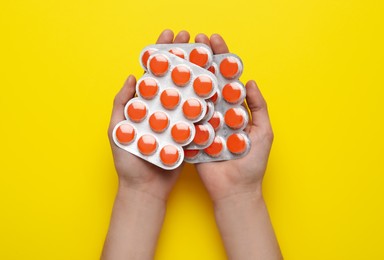 Woman holding blisters with cough drops on yellow background, top view