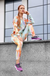 Beautiful woman in gym clothes sitting on parapet on street