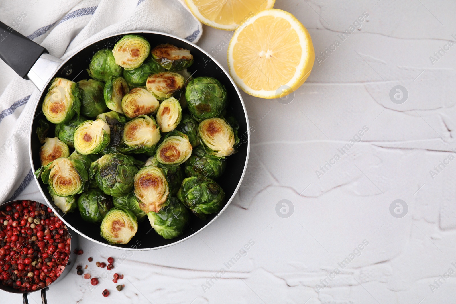 Photo of Delicious roasted Brussels sprouts in frying pan, peppercorns and lemon on white textured table, flat lay. Space for text