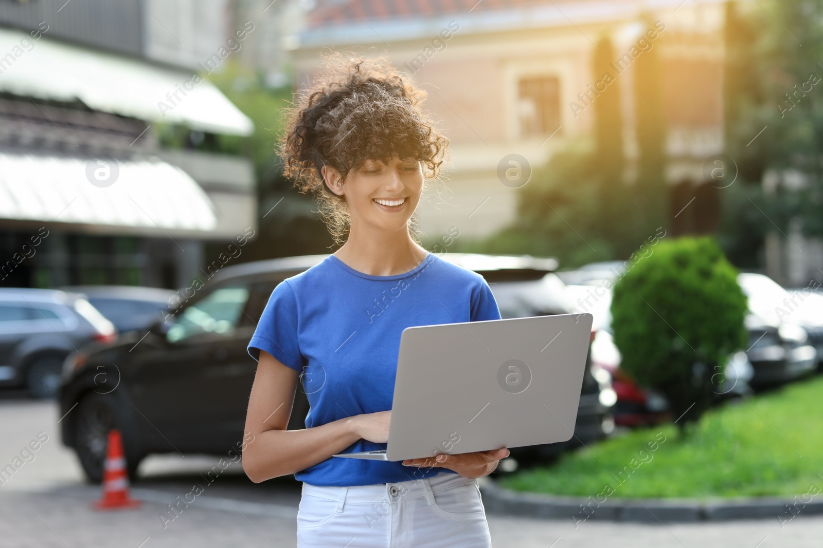 Photo of Happy young woman using modern laptop on city street