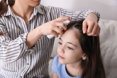 Photo of Mother using lice treatment spray on her daughter's hair indoors