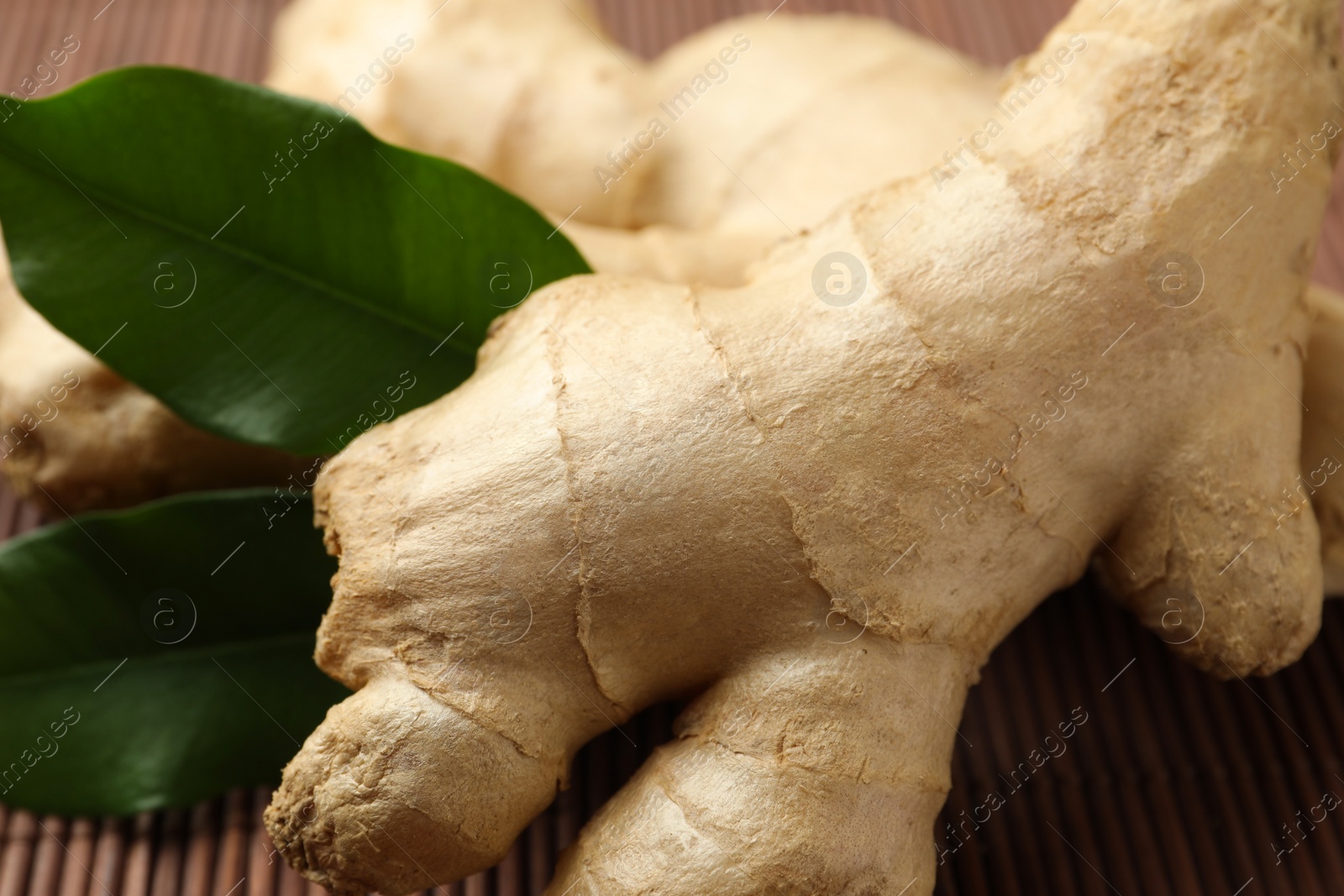 Photo of Fresh ginger with leaves on bamboo mat, closeup