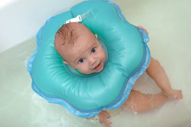 Cute little baby swimming with inflatable ring in bath, above view