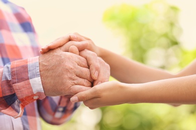 Photo of Young woman holding elderly man hands on blurred background, closeup. Help service