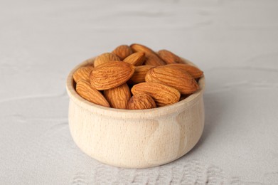 Tasty almonds in wooden bowl on white table