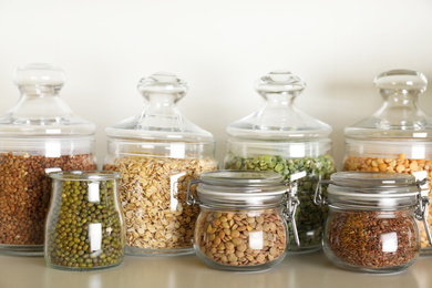 Photo of Different types of legumes and cereals in jars on table. Organic grains