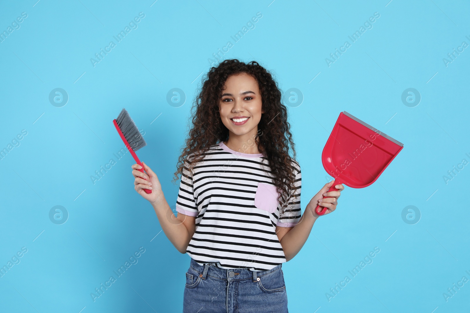Photo of African American woman with broom and dustpan on light blue background