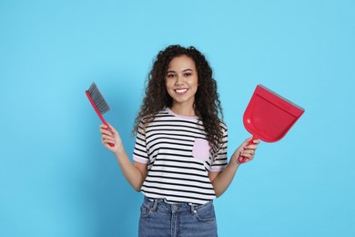 Photo of African American woman with broom and dustpan on light blue background