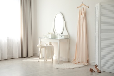 Photo of Beautiful wedding gown hanging near dressing table in room