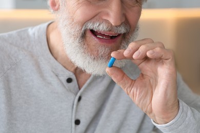 Senior man taking pill on blurred background, closeup