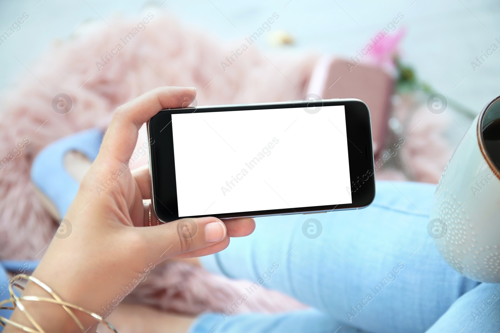 Photo of Young woman holding mobile phone with blank screen in hand, indoors