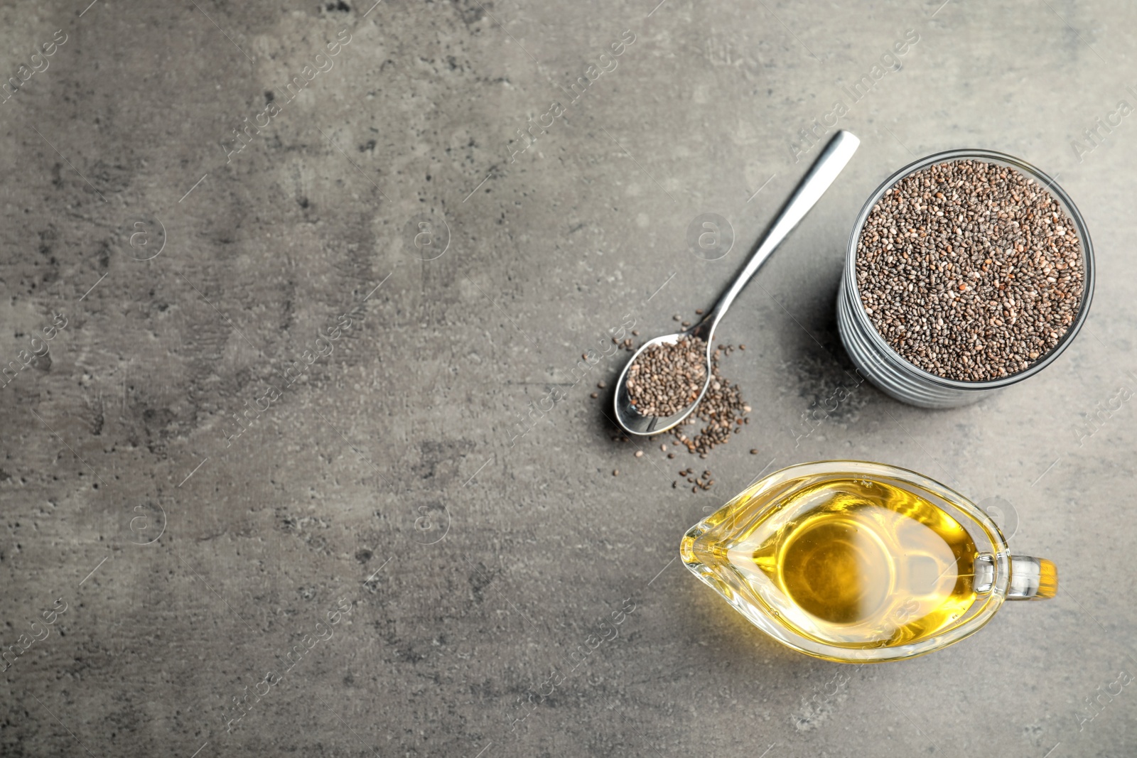Photo of Flat lay composition with sauce boat of oil and chia seeds on grey table. Space for text