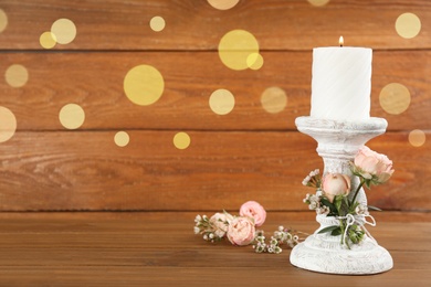 White candlestick with burning candle and floral decor on wooden table. Space for text