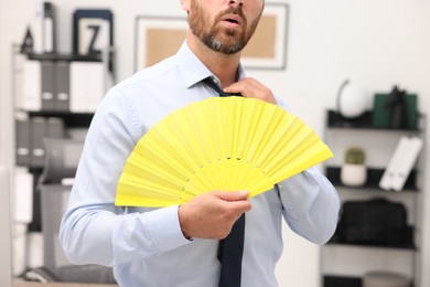 Businessman with yellow hand fan in office, closeup