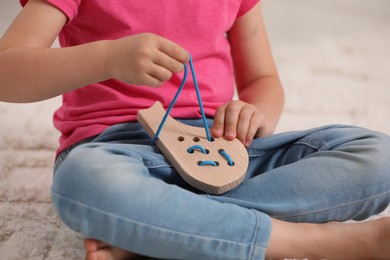 Photo of Little girl playing with wooden lacing toy on carpet indoors, closeup