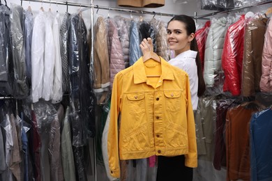 Photo of Dry-cleaning service. Happy worker holding hanger with jacket indoors