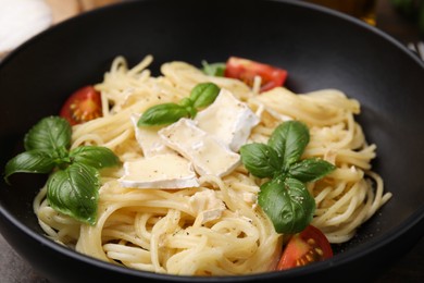 Delicious pasta with brie cheese, tomatoes and basil leaves in bowl, closeup