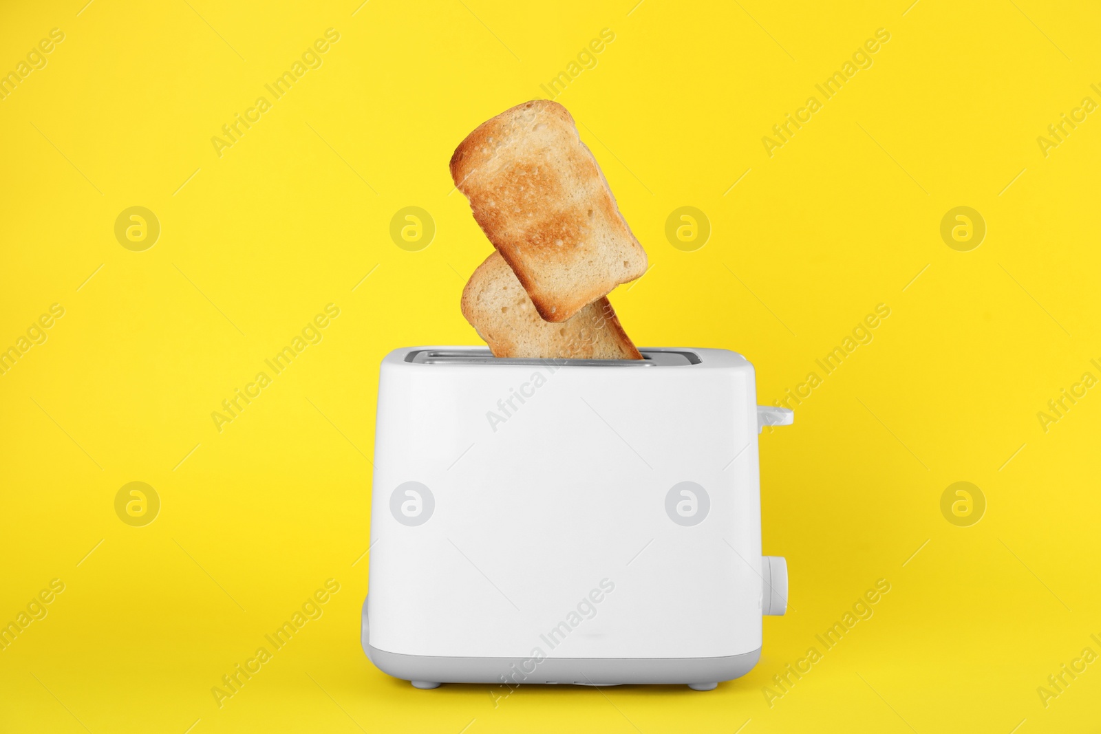 Photo of Bread slices popping up out of electric toaster on yellow background