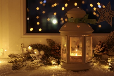 Beautiful Christmas lantern and other decorations on snowy window sill at night