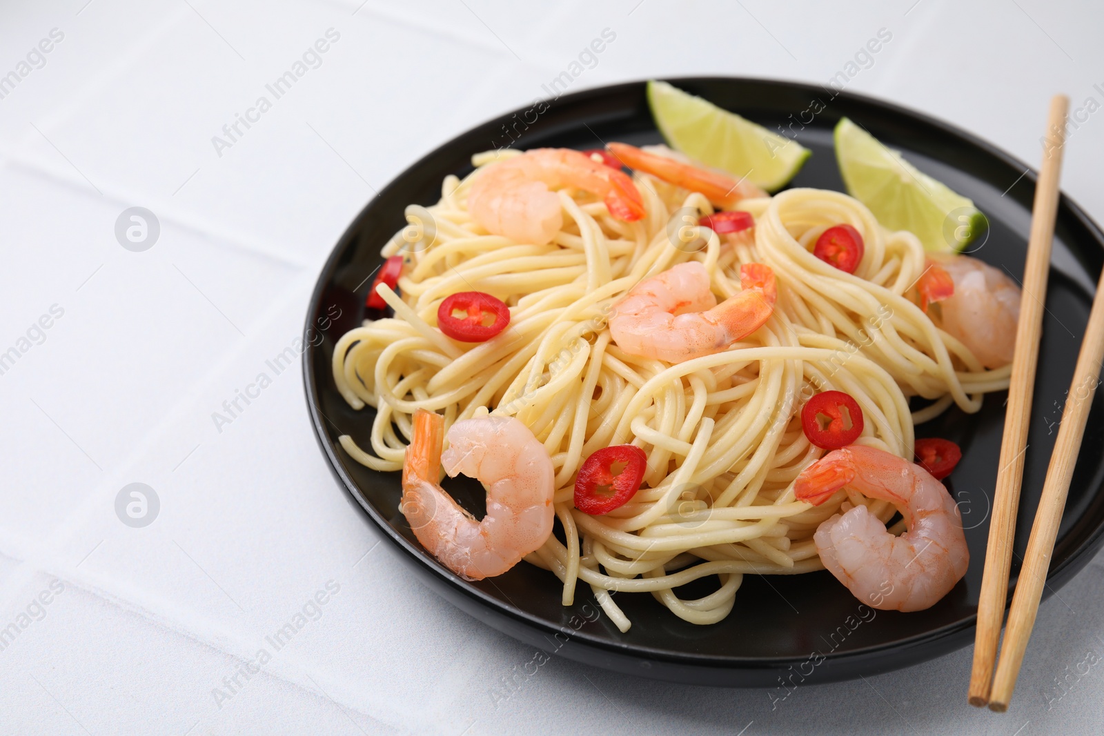 Photo of Tasty spaghetti with shrimps, chili pepper and lime on light tiled table, closeup. Space for text