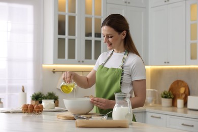 Making bread. Woman pouring oil into bowl at white table in kitchen