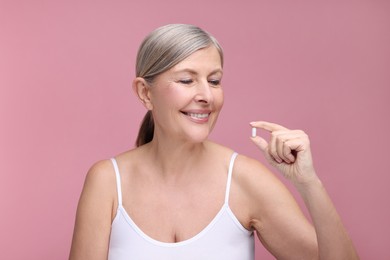 Beautiful woman with vitamin capsule on pink background