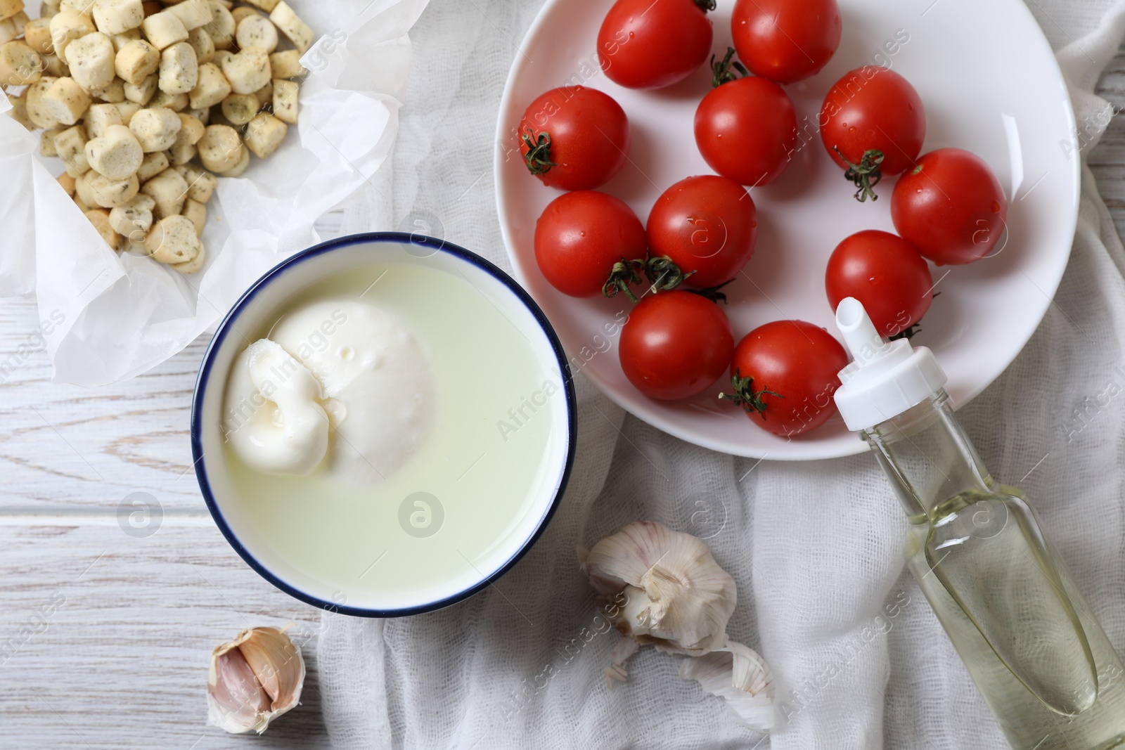 Photo of Delicious burrata cheese served with croutons and tomatoes on white wooden table, flat lay