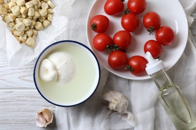 Delicious burrata cheese served with croutons and tomatoes on white wooden table, flat lay