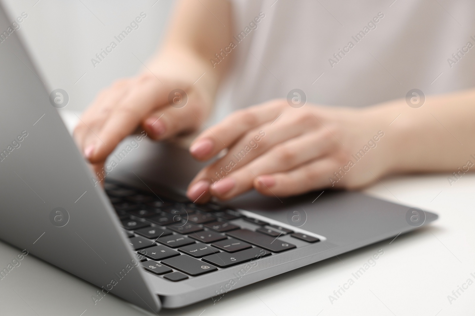 Photo of E-learning. Woman using laptop at white table indoors, closeup