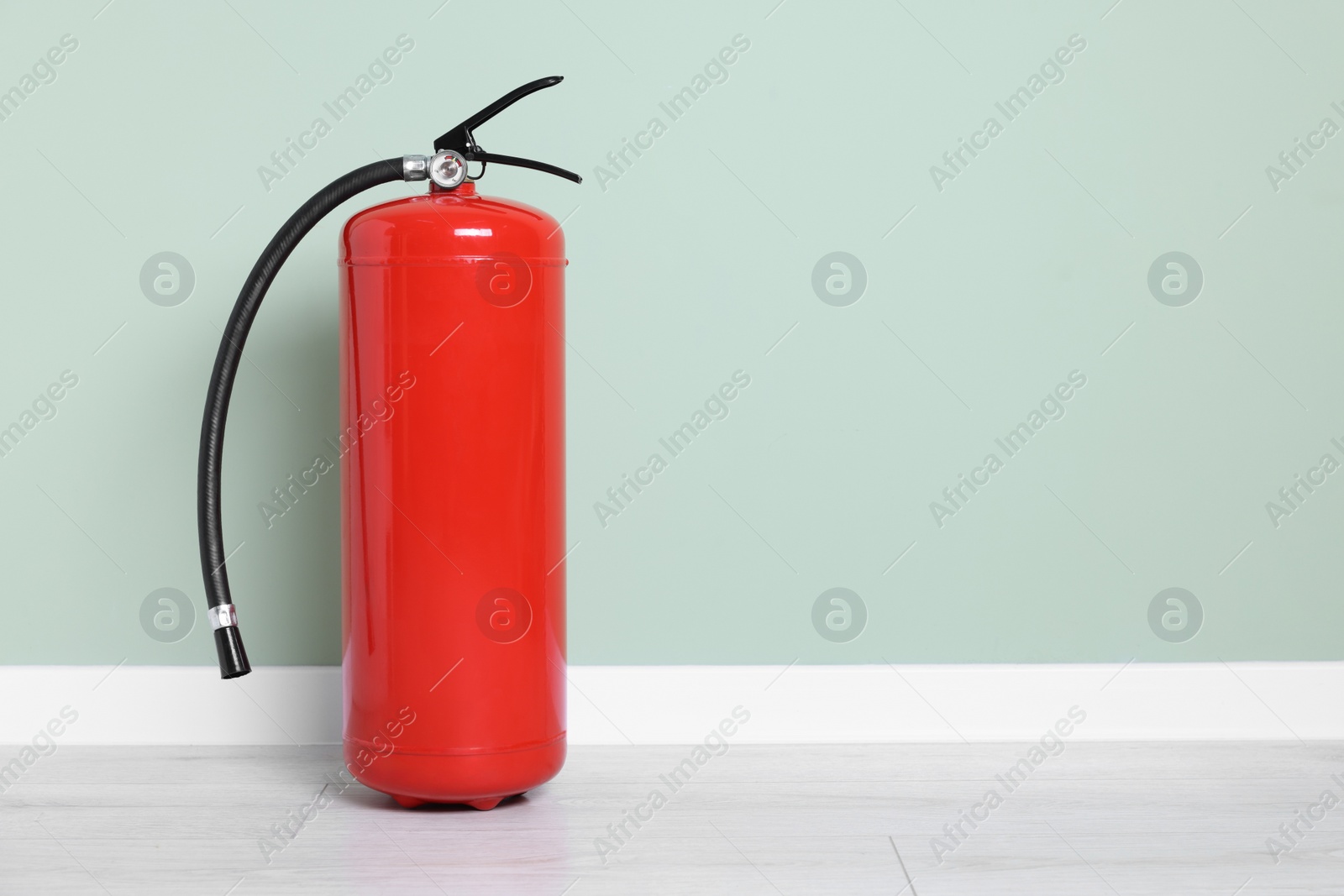 Photo of Red fire extinguisher near light green wall. Space for text