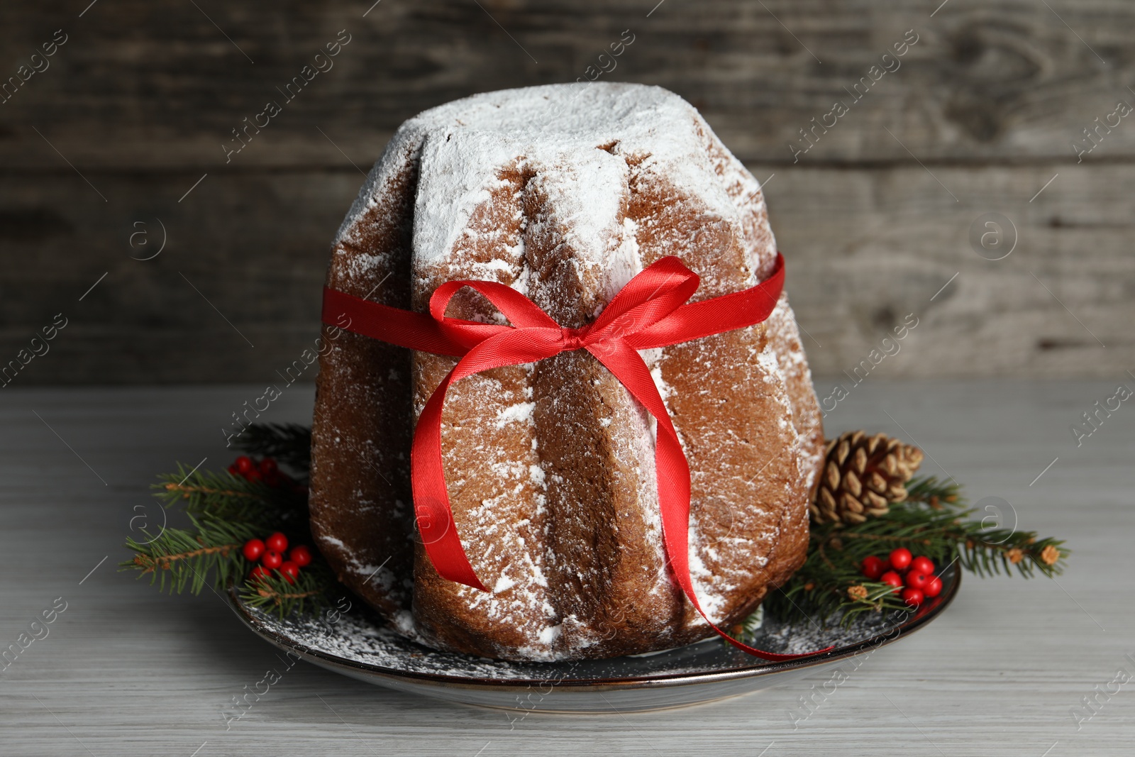 Photo of Delicious Pandoro cake with powdered sugar and red bow, Christmas decor on white wooden table. Traditional Italian pastry