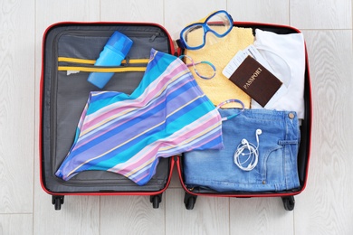 Photo of Open suitcase with female clothing and accessories on wooden background