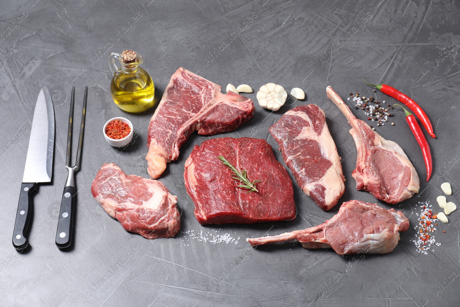 Photo of Fresh raw beef cuts, spices and butcher tools on light grey textured table, above view