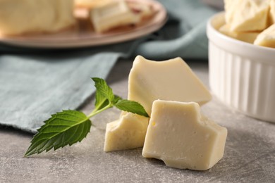 Photo of Pieces of tasty white chocolate and mint on grey table, closeup