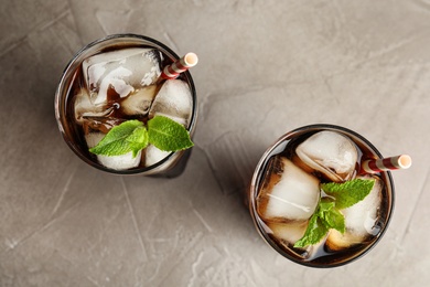 Photo of Glasses of refreshing soda drinks with ice cubes and mint on grey table, flat lay