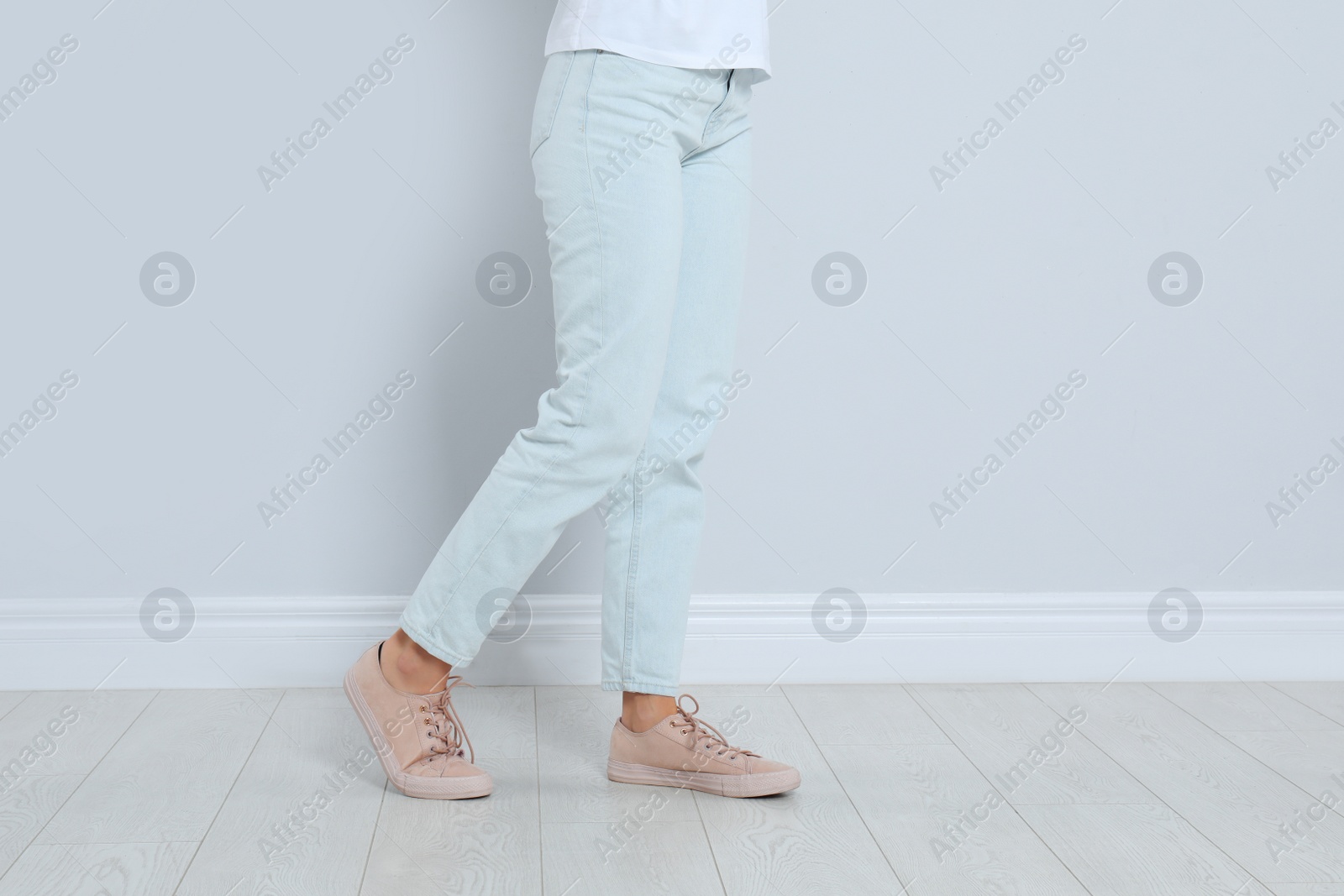 Photo of Young woman in stylish jeans near light wall, closeup