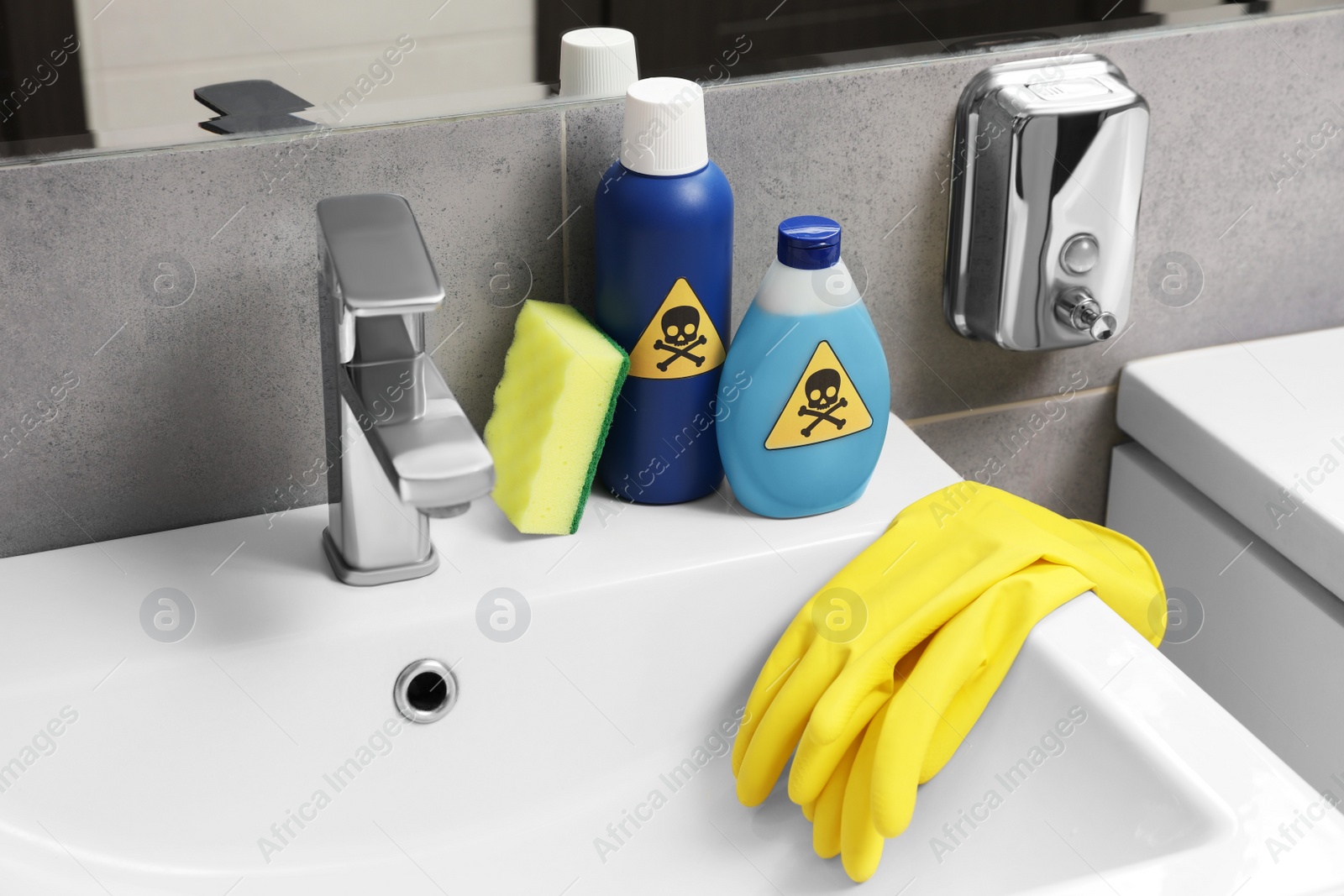 Photo of Bottles of toxic household chemicals with warning signs, gloves and scouring sponge in bathroom