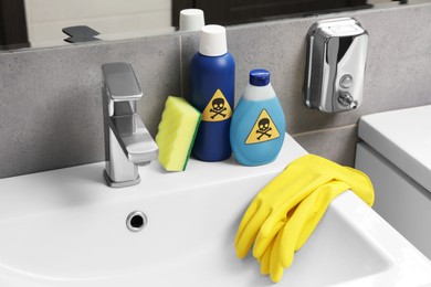 Photo of Bottles of toxic household chemicals with warning signs, gloves and scouring sponge in bathroom