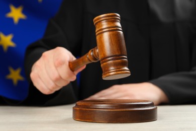 Photo of Judge with gavel at wooden table against flag of European Union, closeup