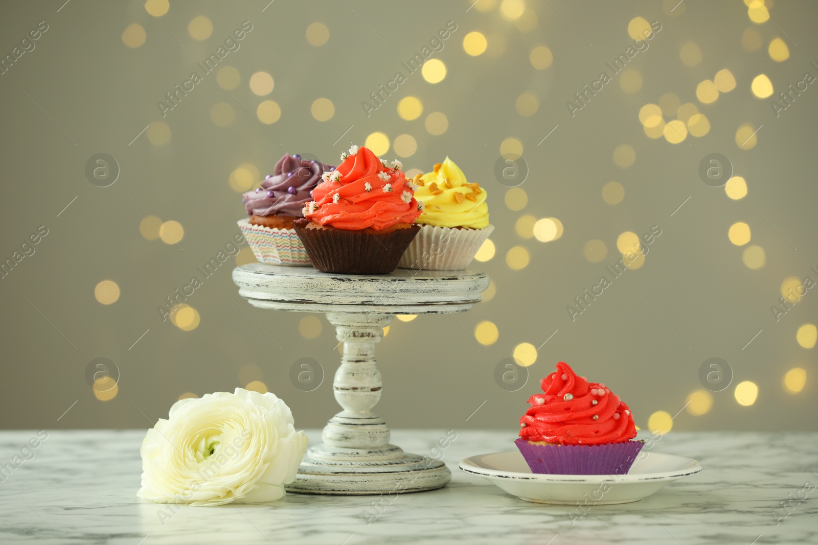 Photo of Different colorful cupcakes on white marble table against blurred lights