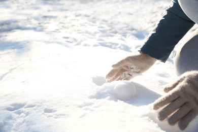 Photo of Woman rolling snowball outdoors on winter day, closeup. Space for text