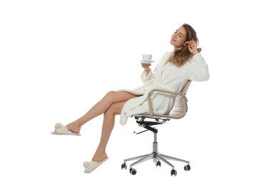 Beautiful young woman wearing bathrobe sitting in chair on white background