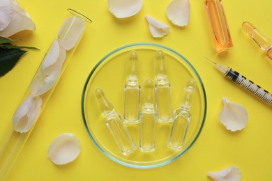 Pharmaceutical ampoules with medication, petals and syringe on yellow background, flat lay