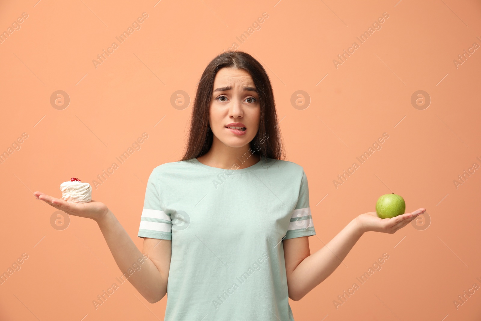 Photo of Woman choosing between apple and cake on orange background